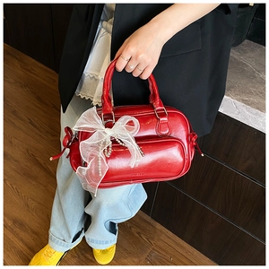Close-up of shiny red Boston bag featuring a large white organza bow and pearl chain detail