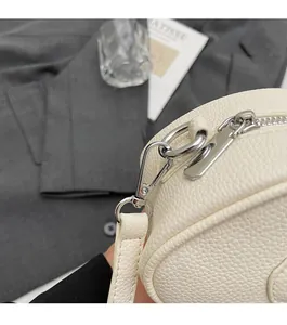 Detail of silver metallic zipper and snap hooks on off-white lychee grain leather handbag