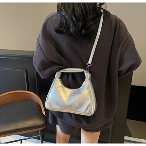 Silver hobo bag with embossed lettering shown in a stylish crossbody carry pose