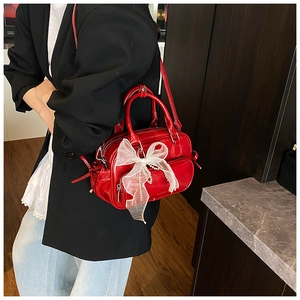 Close-up of red glossy lacquer bag featuring a large white lace bow and pearl chain detail