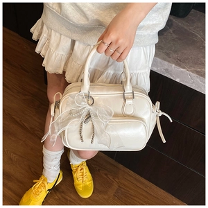 Detail of a cream Boston handbag featuring a lace bow charm and front zipper pocket