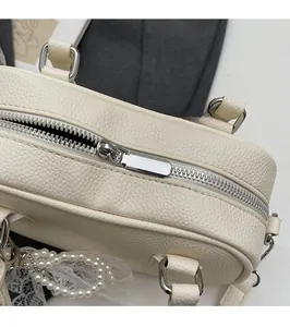 Detailed close-up of smooth silver zipper and pearl lace pendant on beige leather bag