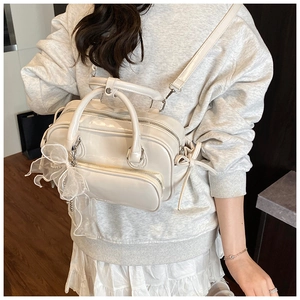 Detail of a creamy white patent leather bag with side bows and a mesh ribbon charm
