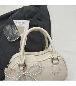 Close-up of cream Boston bag with litchi grain leather and pearl bow charm