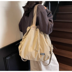 Gros plan d'un sac cabas beige en nylon avec cordon et étiquette porté par un mannequin