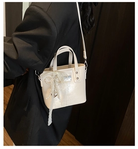 Dettaglio borsa a secchiello crema con fiocco in pizzo e ciondolo di perle su blazer