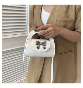 Detail of white mini handbag with silver metal bow and lychee pattern faux leather texture
