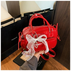 Detail of red patent leather Boston bag with white lace bow and decorative bead chain