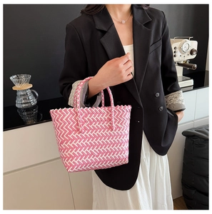 Détail de la texture tressée à chevrons rose et blanc d'un grand sac cabas en paille