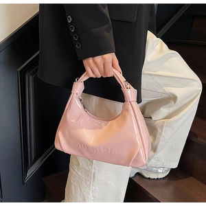 Detail shot of a pink glossy leather hobo bag featuring embossed letters and top handle
