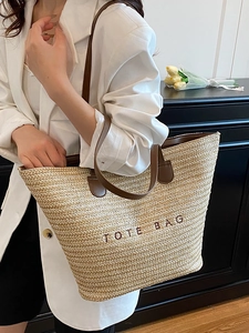Large straw tote bag with brown handles and TOTE BAG embroidery shown on a model