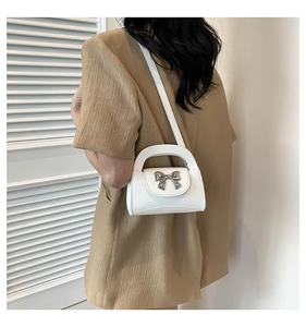 White crossbody bag with silver bow detail worn by a model in a beige suit jacket