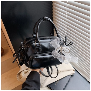 Detail of black glossy faux leather Boston bag with lace bow and pearl charm ornament