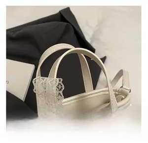Dettaglio dell'elegante bordo in pizzo bianco sulla tracolla della borsa in pelle crema