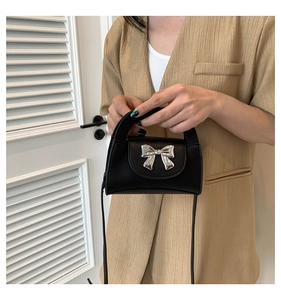 Detail of a black leather mini handbag with a metallic silver bow and crossbody strap