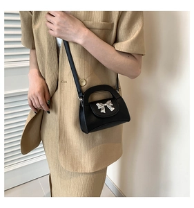 Detail of black pebbled leather crossbody bag with metallic silver bow worn by a model