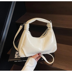 Detail of a creamy white crescent hobo bag with embossed lettering on smooth glossy leather