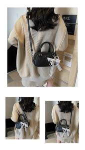 Close-up of black Boston bag with lychee texture and elegant white lace bow charm