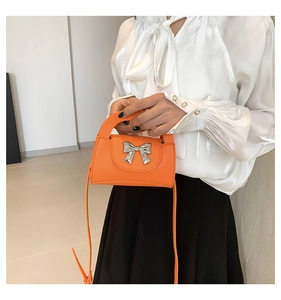 Detail of orange lychee leather crossbody bag with silver metal bow and top handle