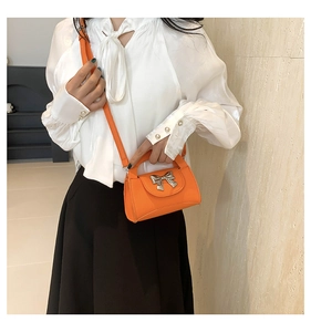 Detail view of orange crossbody bag with a silver metal bow accent and lychee texture