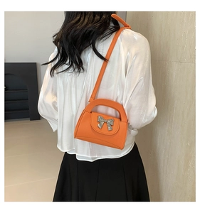 Detail of orange pebble leather crossbody bag with a metallic silver bow on the back of model