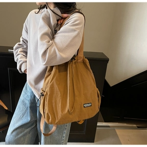 Détail du sac bandoulière en toile caramel montrant la texture et le logo de la marque DOUCU