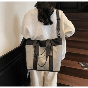 Large gray nylon crossbody tote bag shown on a model in a modern urban staircase setting