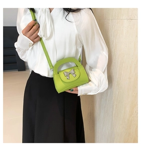 Detail of green leather handbag featuring a large silver bow and lychee texture