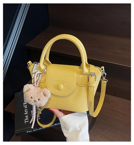 Détail d'un sac à main jaune en cuir avec breloque d'ours en peluche et poignée