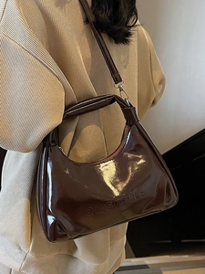 Brown wax leather top handle bag with embossed letters for women shown on model shoulder