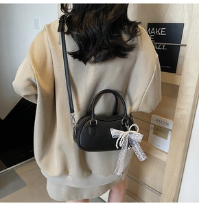 Close-up of black lychee leather mini Boston bag with white lace bow and pearl charm