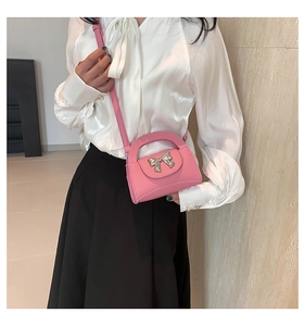 Detail of pink mini crossbody bag with silver bow accent and pebbled leather texture