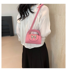 Detail of pink pebbled leather mini bag with silver bow buckle on model shoulder