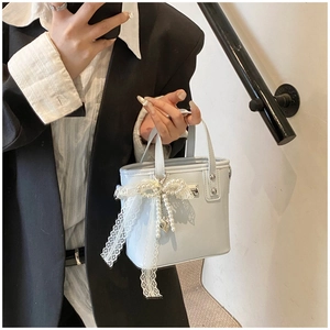 Dettaglio della borsa a secchiello azzurra con elegante ciondolo in perle e fiocco in pizzo