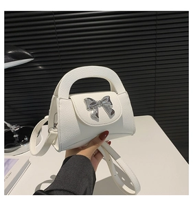 Detailed view of white lychee leather mini bag with silver metal bow and shoulder strap