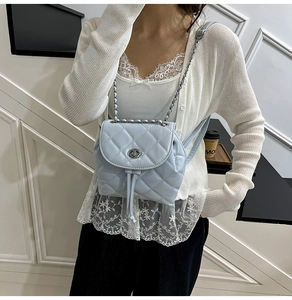 Close-up of a light blue quilted mini backpack with silver chain strap worn by a model