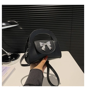 Detail of black pebbled leather mini bag with a metallic silver bow and top handle