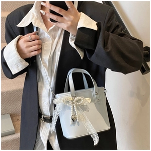 Dettaglio della borsa a secchiello azzurra con fiocco in pizzo bianco e catena di perle