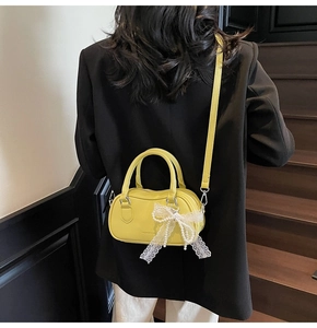Detail of yellow lychee leather Boston bag with white lace bow and pearl decoration