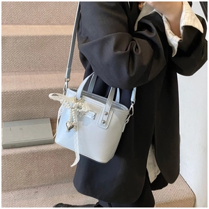 Dettaglio della mini borsa a secchiello azzurra con fiocco in pizzo, perle e cuore