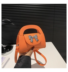Detail view of bright orange pebble grain leather handbag with silver metal bow clasp