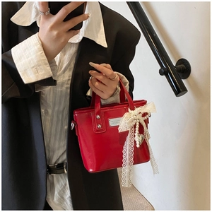 Detail of red patent leather bucket bag with lace bow and pearl heart charm