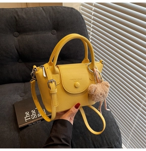 Détail d'un sac à main jaune vif en cuir grainé avec un pendentif ours et une poignée