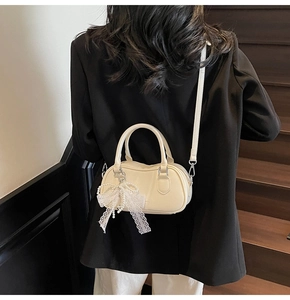Detail of cream white mini Boston bag with lace bow charm and pearl accent on a model