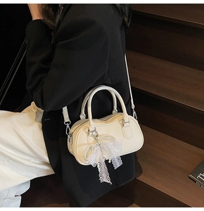 Detail of cream Boston bag with lychee texture and pearl lace bow charm on model