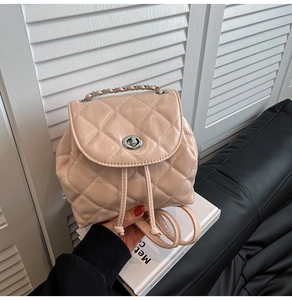 Detail view of small beige quilted backpack with silver metal twist lock and chain strap