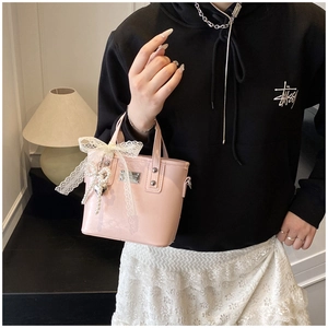 Pink glossy bucket bag with lace bow and pearl heart pendant held by a model