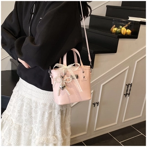 Dettaglio borsa in pelle verniciata rosa con fiocco in pizzo e ciondolo di perle