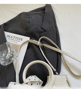 Détail du sac seau en cuir grainé blanc avec foulard à pois enroulé sur l'anse