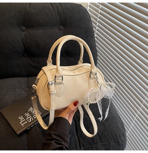 Close-up of cream Boston bag with litchi texture, lace bow charm, and silver hardware